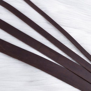 May include: Four strips of dark brown leather arranged in a fan shape on a white surface.