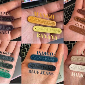 Puede incluir: Una colecci&oacute;n de etiquetas de cuero en varios colores, incluyendo burdeos, marsala, mango, pl&aacute;tano, co&ntilde;ac, marr&oacute;n, caramelo, verde oscuro, verde, verde hierba, &iacute;ndigo, azul vaquero, latte y leche de seda. Cada etiqueta tiene el texto "Зроблено руками" (que significa "Hecho a mano") grabado en relieve.