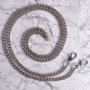 May include: A silver chain with two lobster clasps. The chain is double-layered and has a curb link design.