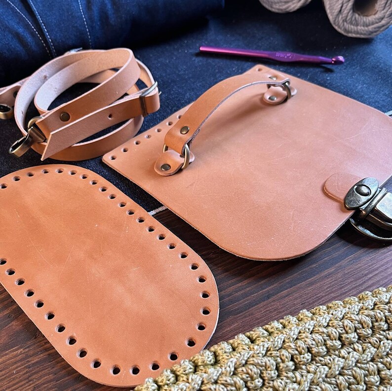 May include: A set of brown leather pieces for crafting a bag. The pieces include a handle, a flap with a buckle, and two oval-shaped pieces with holes around the edges.
