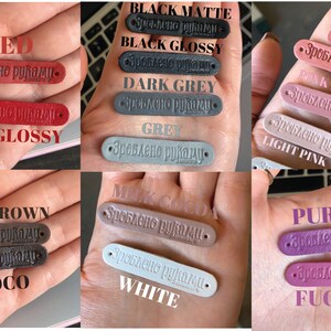 Puede incluir: Una colecci&oacute;n de etiquetas de cuero en varios colores, incluyendo rojo, negro, gris, coral, rosa, marr&oacute;n, blanco y morado. Cada etiqueta tiene el texto "Зроблено руками" (que significa "Hecho a mano") grabado en relieve.