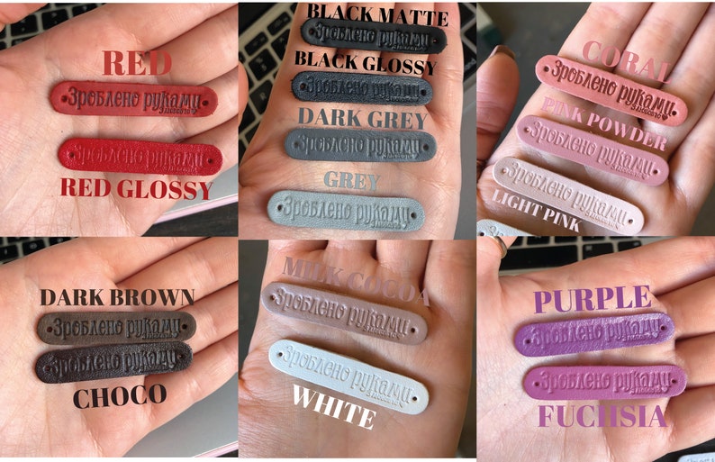 Puede incluir: Una colecci&oacute;n de etiquetas de cuero en varios colores, incluyendo rojo, negro, gris, coral, rosa, marr&oacute;n, blanco y morado. Cada etiqueta tiene el texto "Зроблено руками" (que significa "Hecho a mano") grabado en relieve.