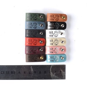 May include: A set of 10 leather tags with the words "Fait Main" and a heart-shaped hand design. The tags are in various colors, including green, blue, black, white, red, burgundy, and teal.