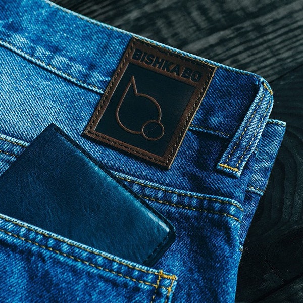 May include: A blue denim pocket with a black leather wallet and a brown leather patch with the text "BISHKA BO" in white.