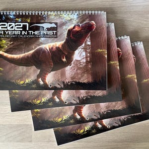 Pode incluir: Um calendário de parede em espiral de 2021 intitulado A Year in the Past de Andy Frazer. A capa apresenta um grande Tyrannosaurus Rex castanho numa floresta. O texto 2021 A Year in the Past Paleoart Calendar Andy Frazer está impresso a branco.