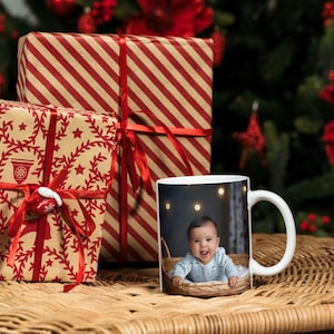 A scene with some christmas presents wrapped up with a mug with a picutre of a smiling baby with bright blue eyesall on a wicker table top