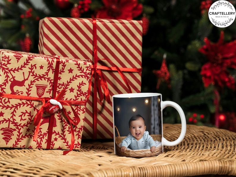 A scene with some christmas presents wrapped up with a mug with a picutre of a smiling baby with bright blue eyesall on a wicker table top