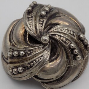 Peut inclure: Une broche en m&eacute;tal argent&eacute; avec un design abstrait tourbillonnant. La broche est compos&eacute;e de plusieurs pi&egrave;ces superpos&eacute;es qui cr&eacute;ent un effet tridimensionnel.