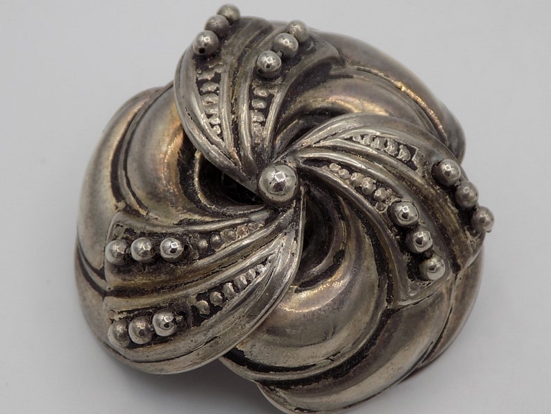 Peut inclure: Une broche en m&eacute;tal argent&eacute; avec un design abstrait tourbillonnant. La broche est compos&eacute;e de plusieurs pi&egrave;ces superpos&eacute;es qui cr&eacute;ent un effet tridimensionnel.