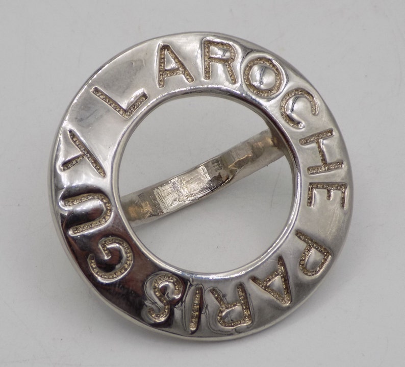 May include: A silver ring with the words "LA ROCHE PARIS" engraved around the band.