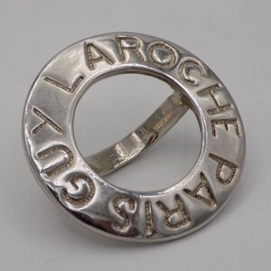May include: A silver ring with the words "Laroche Paris" engraved around the band.