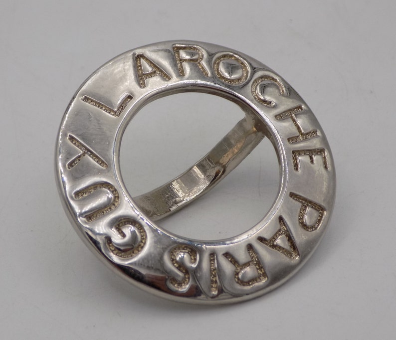 May include: A silver ring with the words "Laroche Paris" engraved around the band.