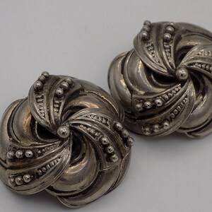 Peut inclure: Une paire de boucles d'oreilles argent&eacute;es avec un motif en spirale. Les boucles d'oreilles sont en m&eacute;tal et ont une surface textur&eacute;e.