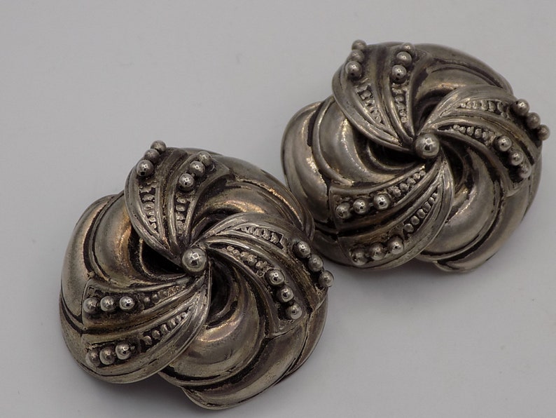 Peut inclure: Une paire de boucles d'oreilles argent&eacute;es avec un motif en spirale. Les boucles d'oreilles sont en m&eacute;tal et ont une surface textur&eacute;e.