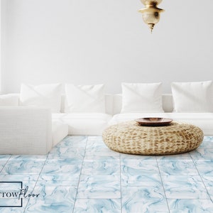 Peut inclure: Un canapé sectionnel blanc avec des coussins blancs est posé sur un sol en carrelage de marbre bleu clair. Un ottoman en osier tressé avec un bol en bois se trouve devant le canapé. Le texte "Sparrow Floor" est dans le coin inférieur gauche de l'image.