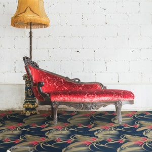 Puede incluir: Una chaise longue roja con un marco de madera oscura se encuentra sobre un suelo estampado en azul marino y dorado. El suelo tiene un patrón repetitivo de hojas y flores estilizadas.