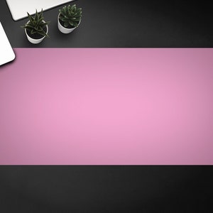 May include: A pink desk mat on a black surface. There is a laptop and two small potted plants on the surface.