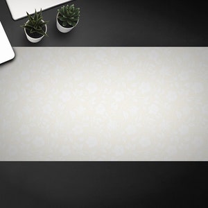 May include: A white desk mat with a subtle floral pattern. The mat is on a black surface with a laptop and two potted plants.
