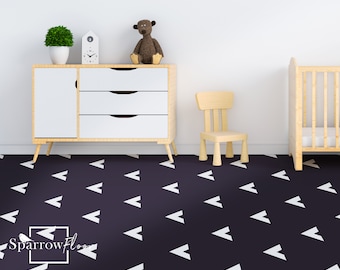 May include: A white and black arrow patterned floor covering in a nursery with a white dresser, a wooden chair, and a crib.
