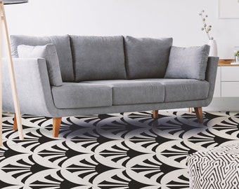 Puede incluir: Un sofá gris con tres cojines se encuentra sobre un suelo con estampado geométrico en blanco y negro. Un pequeño puf con estampado geométrico en blanco y negro se encuentra en primer plano. El patrón del suelo es un diseño repetitivo de formas de abanico en blanco y negro.