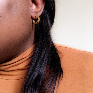 May include: A close-up of a person's ear wearing a gold hoop earring. The earring has a textured design.