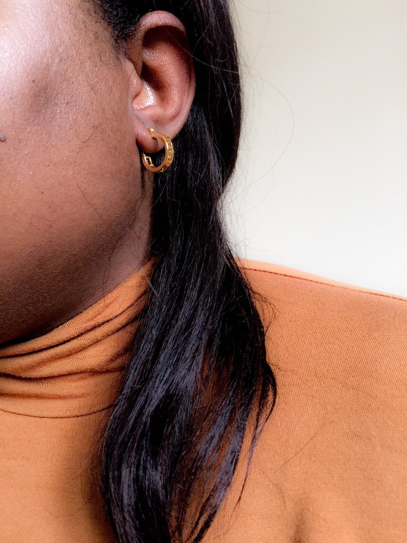 May include: A close-up of a person's ear wearing a gold hoop earring. The earring has a textured design.