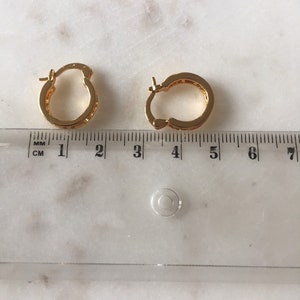 May include: A pair of gold hoop earrings with a small diameter, measuring approximately 1.5 inches in diameter. The earrings are made of a shiny metal and have a smooth finish.
