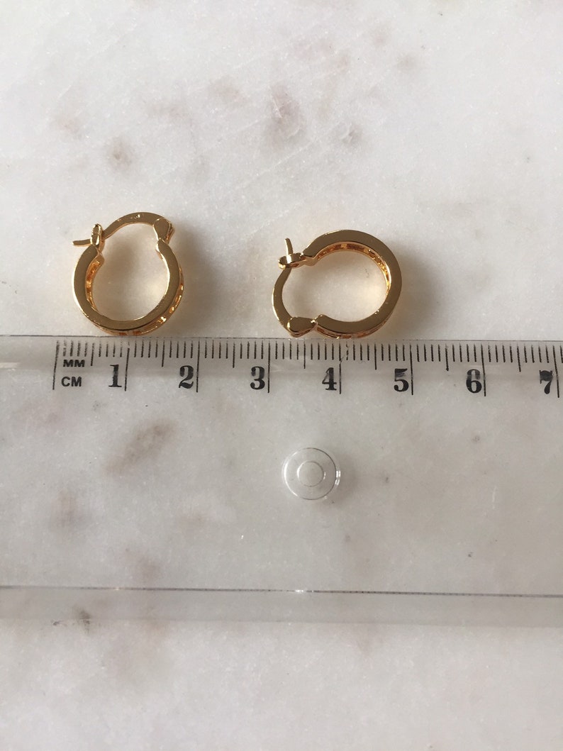May include: A pair of gold hoop earrings with a small diameter, measuring approximately 1.5 inches in diameter. The earrings are made of a shiny metal and have a smooth finish.