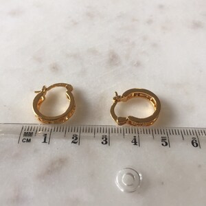 May include: A pair of gold hoop earrings with a textured design. The earrings are approximately 1.5 inches in diameter.