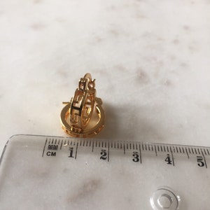 May include: Gold hoop earrings with a geometric design. The earrings are approximately 2 cm in diameter.