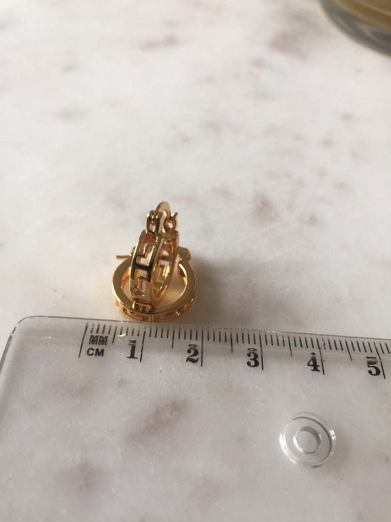May include: Gold hoop earrings with a geometric design. The earrings are approximately 2 cm in diameter.