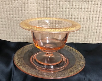 May include: A pink glass bowl with a gold rim and a matching pink glass plate. The bowl and plate feature a delicate floral design.