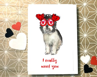 Puede incluir: Una tarjeta blanca con una ilustración en blanco y negro de un perro que lleva gafas de sol en forma de corazón rojo y pompones rojos en las orejas. El texto "I really woof you" está escrito en rojo debajo del perro.