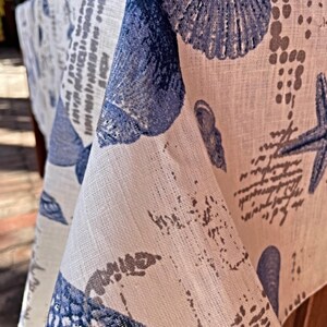 May include: A white linen tablecloth with a blue and gray seashell pattern. The tablecloth features a variety of seashells, including clams, oysters, and mussels. The tablecloth is perfect for a coastal-themed dinner party or a casual summer gathering.