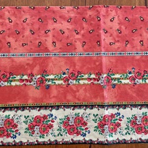 Peut inclure: Un tissu rectangulaire à motifs floraux dans les tons de rouge, rose et crème. Le motif présente des motifs floraux et géométriques répétés. Le tissu est probablement destiné à la décoration intérieure ou aux projets d'artisanat.