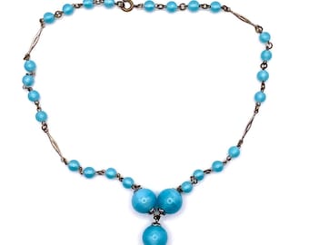 May include: A vintage necklace featuring light blue beads and silver-toned metal accents. The necklace has a delicate design with a central cluster of three larger beads and a single pendant bead. The necklace is secured with a clasp.