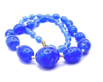 May include: A vintage blue beaded necklace with a swirl pattern. The necklace features various sizes of oval-shaped beads, strung together with a silver clasp. The beads have a glossy finish and a marbled effect.