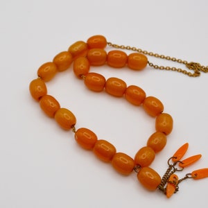 Puede incluir: Un collar de cuentas de ámbar con una cadena de oro y borlas naranjas. Las cuentas son de forma ovalada y tienen un acabado brillante.