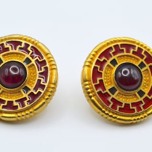 May include: A pair of gold-tone earrings with red and black enamel and a dark red gemstone in the centre.