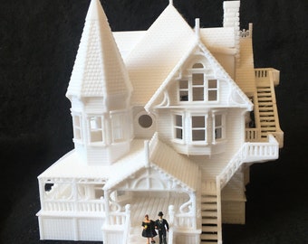 May include: A white 3D printed model of a Victorian house with a pointed roof, a wraparound porch, and a couple standing on the steps.
