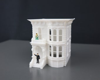 May include: A white 3D printed model of a Victorian-style house with a small figure standing on the porch and another figure on the balcony.