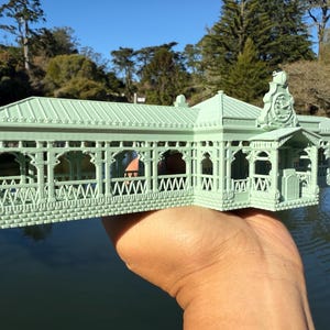 May include: A detailed model of a green, ornate building with a clock tower. The model is made of plastic and has a brick base. The building has a series of arches and windows.