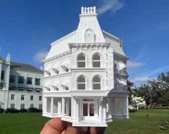 May include: A white 3D printed model of a Victorian-style building with a gabled roof, four stories, and a storefront. The model has detailed brickwork, windows, and a door.