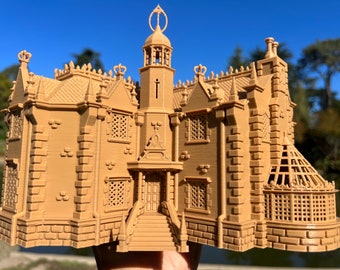 May include: A tan-colored miniature model of a stately building with intricate architectural details. The model features multiple stories, decorative windows, and a central tower with a spire. The building has a detailed facade and is likely a decorative item.