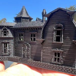 May include: A black 3D printed model of a house with a pointed roof, multiple windows, and a brick foundation.