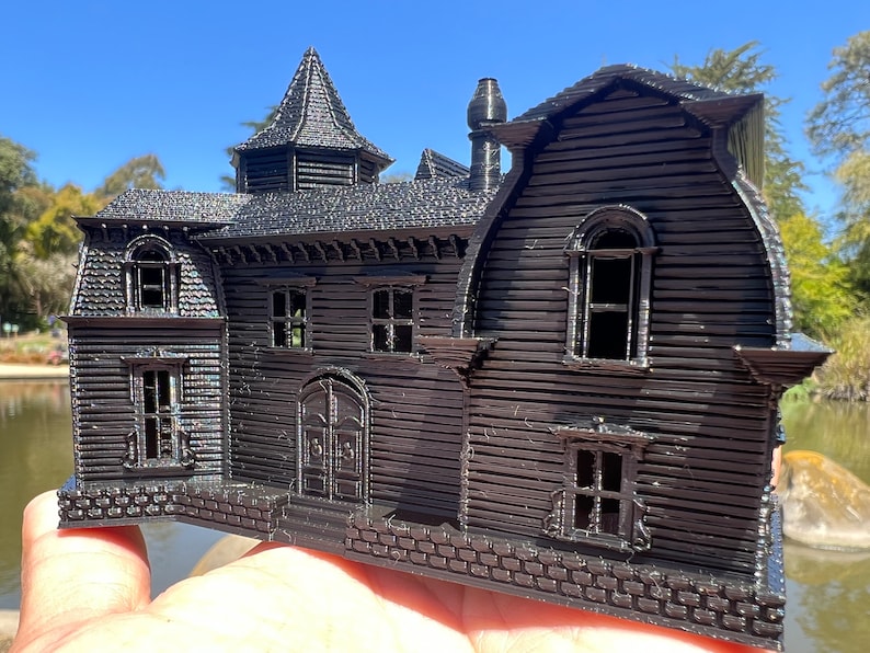 May include: A black 3D printed model of a house with a pointed roof, multiple windows, and a brick foundation.