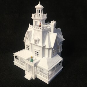 May include: A white 3D printed model of a Victorian style house with a tower and a porch. The model is detailed with windows, doors, and a roof.