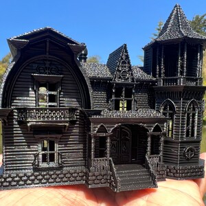 May include: A black 3D printed model of a Victorian style house with a tower, a porch, and a stone foundation.