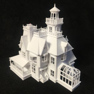 May include: A white 3D printed model of a Victorian-style house with a tower and a greenhouse addition. The house has a porch and multiple windows.