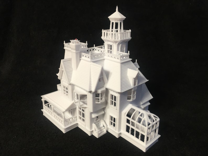 May include: A white 3D printed model of a Victorian-style house with a tower and a greenhouse addition. The house has a porch and multiple windows.